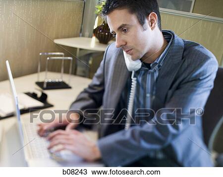 Stock Image - Close-up of a businessman using a laptop and talking on the telephone. Fotosearch