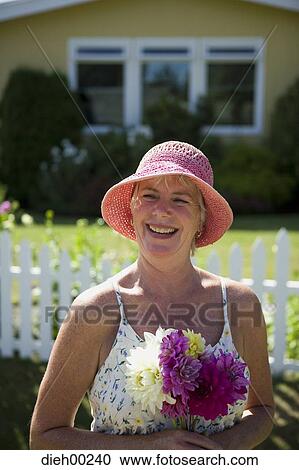 Stock Image - Close-up of a mature woman holding a bunch of flowers and smiling. Fotosearch