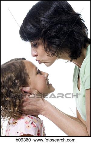 Stock Image - Close-up of a mid adult woman kissing her daughter's forehead. Fotosearch