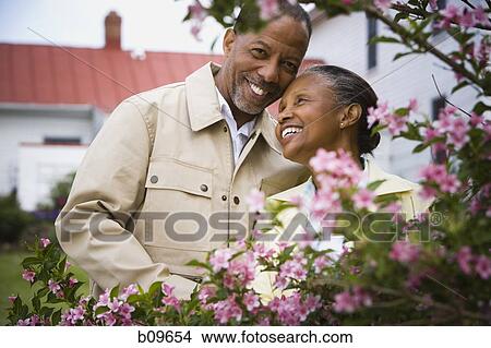 Picture - Close-up of a senior man and a senior woman smiling behind flowers. Fotosearch