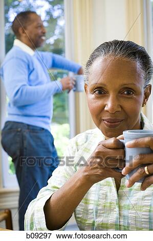 Close-up of a senior woman holding a cup of coffee with a senior man standing behind her View Large Photo Image Stock Photo - Close-up of a senior woman holding a cup of coffee with a senior man standing behind her. Fotosearch