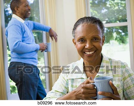 Close-up of a senior woman holding a cup of coffee with a senior man standing behind her View Large Photo Image Stock Photograph - Close-up of a senior woman holding a cup of coffee with a senior man standing behind her. Fotosearch