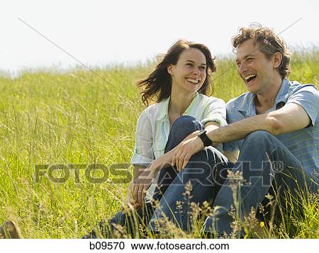 Stock Image - Close-up of a woman and a man sitting together and laughing in a field. Fotosearch