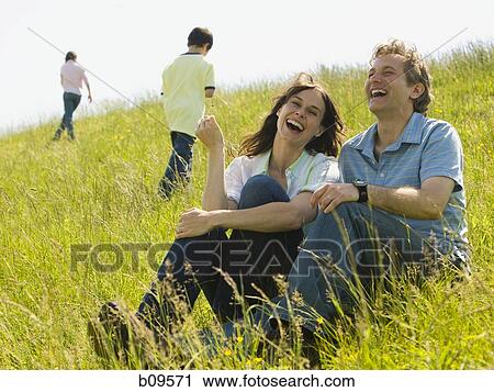 Close-up of a woman and a man sitting together and laughing in a field View Large Photo Image Stock Image - Close-up of a woman and a man sitting together and laughing in a field. Fotosearch