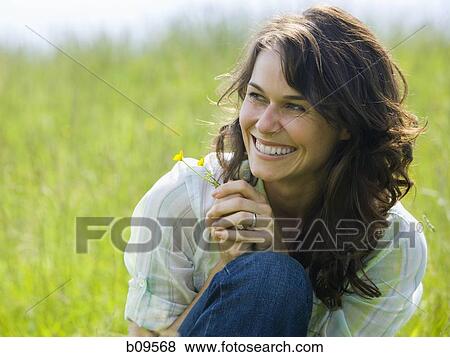 Close-up of a woman holding a flower in a field View Large Photo Image Stock Photo - Close-up of a woman holding a flower in a field. Fotosearch