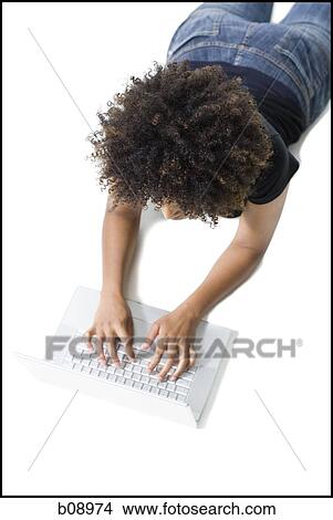 Picture - Close-up of a young woman lying on the floor and using a laptop. Fotosearch