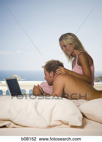 Stock Image - Couple relaxing on terrace looking at laptop. Fotosearch