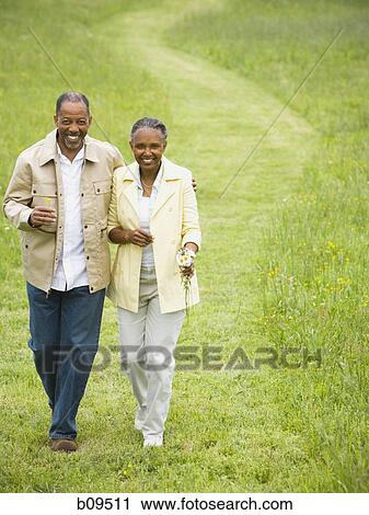 Stock Image - High angle view of a senior man and a senior woman walking in a field. Fotosearch