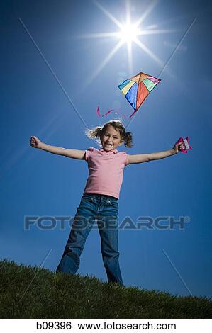Stock Photograph - Low angle view of a girl flying a kite. Fotosearch
