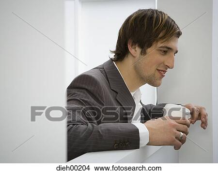 Picture - Male office worker leaning over divider and holding coffee. Fotosearch