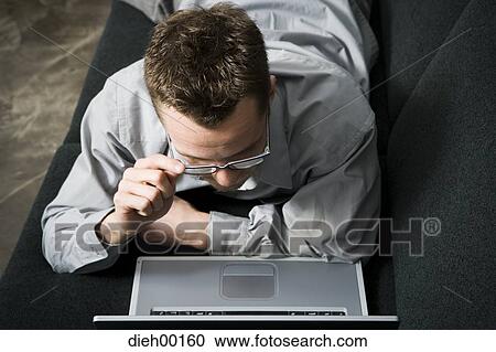 Stock Image - Male office worker on couch working on laptop. Fotosearch