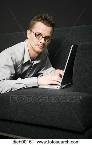 Male office worker on couch working on laptop View Large Photo Image Stock Image - Male office worker on couch working on laptop. Fotosearch
