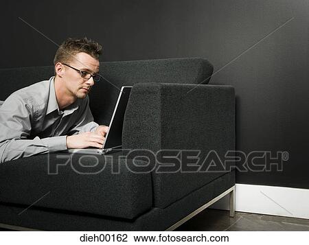 Male office worker on couch working on laptop View Large Photo Image Stock Image - Male office worker on couch working on laptop. Fotosearch