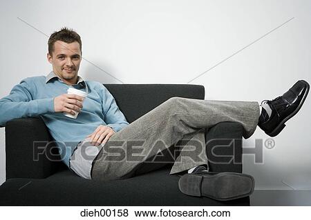 Male office worker reclining on couch and holding coffee View Large Photo Image Stock Photo - Male office worker reclining on couch and holding coffee. Fotosearch