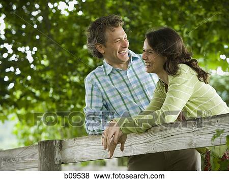 Stock Photo - man and a woman leaning on a wooden fence. Fotosearch