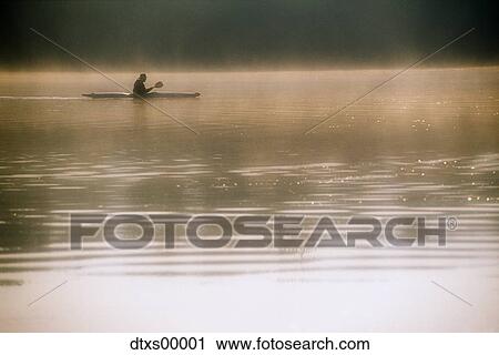 Stock Image - Man canoeing on quiet lake. Fotosearch