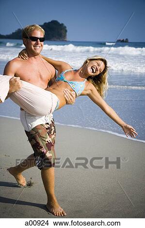 Picture - Man carrying girlfriend on beach. Fotosearch