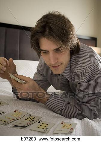 Stock Image - Man in hotel room playing solitaire. Fotosearch
