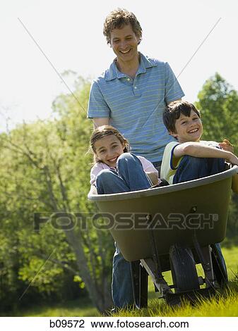 man pushing his son and daughter in a wheelbarrow View Large Photo Image Stock Image - man pushing his son and daughter in a wheelbarrow. Fotosearch