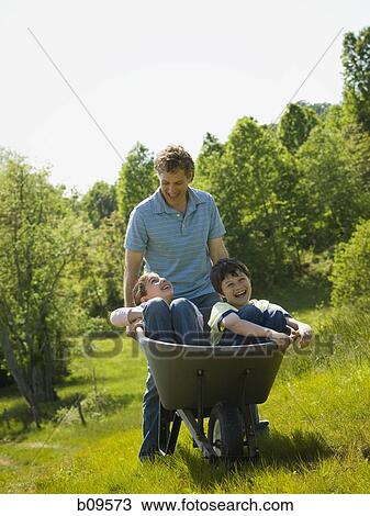 man pushing his son and daughter in a wheelbarrow View Large Photo Image Stock Image - man pushing his son and daughter in a wheelbarrow. Fotosearch