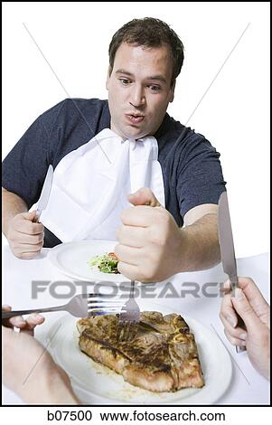 Stock Image - Overweight man stealing steak off partner's plate. Fotosearch