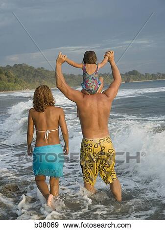 Stock Photo - Parents playing with young daughter on beach. Fotosearch
