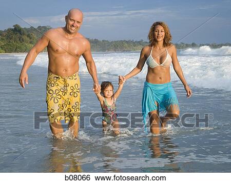 Stock Photograph - Parents playing with young daughter on beach. Fotosearch