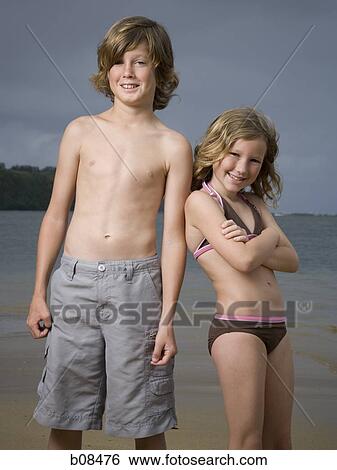 Stock Photograph - Portrait of a boy and his sister standing on the beach. Fotosearch