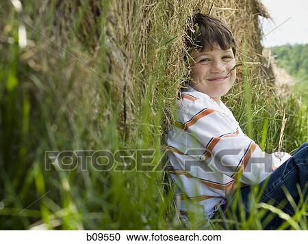 Stock Image - Portrait of a boy sitting against a hay bale. Fotosearch