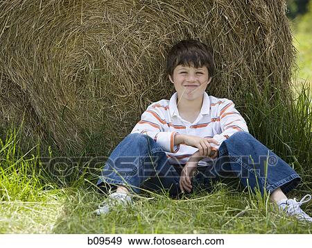 Stock Photo - Portrait of a boy sitting against a hay bale. Fotosearch