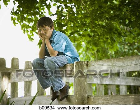 Picture - Portrait of a boy sitting on a wooden fence. Fotosearch