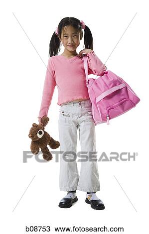 Stock Image - Portrait of a girl holding a teddy bear and a schoolbag. Fotosearch