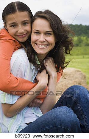 Stock Image - Portrait of a girl hugging her mother from behind. Fotosearch