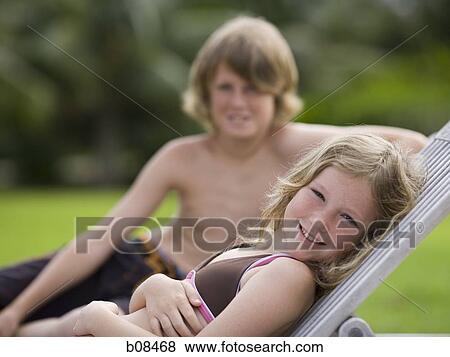 Portrait of a girl reclining on a lounge chair with her brother behind her View Large Photo Image Stock Photo - Portrait of a girl reclining on a lounge chair with her brother behind her. Fotosearch
