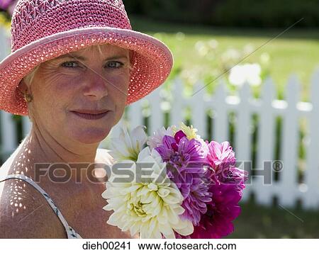 Stock Image - Portrait of a mature woman holding a bunch of flowers and smiling. Fotosearch