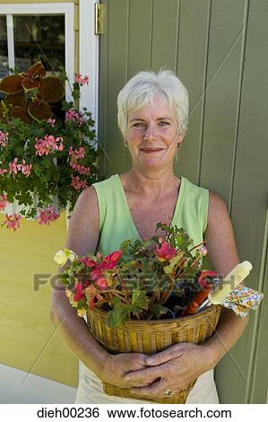Stock Photograph - Portrait of a mature woman holding a basket of flowers and smiling. Fotosearch