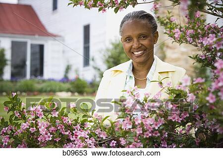 Stock Image - Portrait of a mature woman smiling behind flowers. Fotosearch