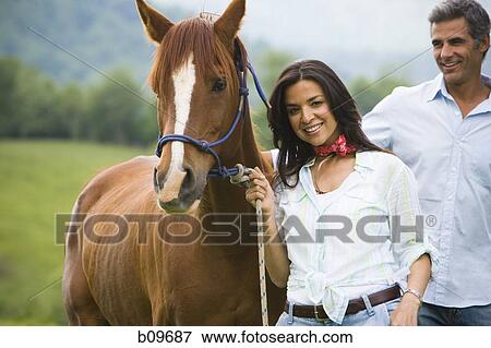 Portrait of a woman holding the reins of a horse with a man beside her View Large Photo Image Stock Photo - Portrait of a woman holding the reins of a horse with a man beside her. Fotosearch
