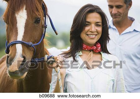 Portrait of a woman holding the reins of a horse with a man beside her View Large Photo Image Stock Photo - Portrait of a woman holding the reins of a horse with a man beside her. Fotosearch