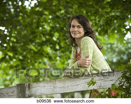 Portrait of a woman leaning on a wooden fence View Large Photo Image Stock Photograph - Portrait of a woman leaning on a wooden fence. Fotosearch
