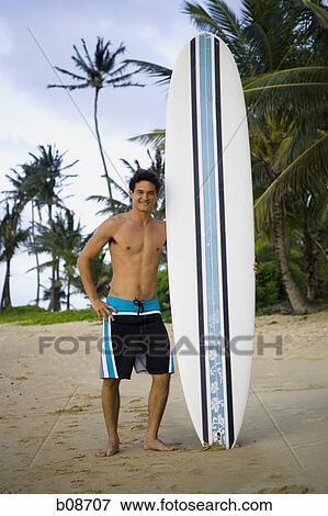 Stock Photo - Portrait of a young couple holding a surfboard on the beach. Fotosearch