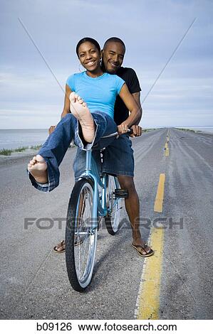 Portrait of a young couple sitting on a bicycle View Large Photo Image Stock Photograph - Portrait of a young couple sitting on a bicycle. Fotosearch