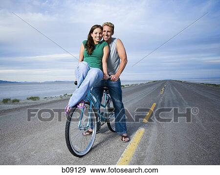 Portrait of a young woman and a mid adult man sitting on a bicycle View Large Photo Image Stock Photo - Portrait of a young woman and a mid adult man sitting on a bicycle. Fotosearch