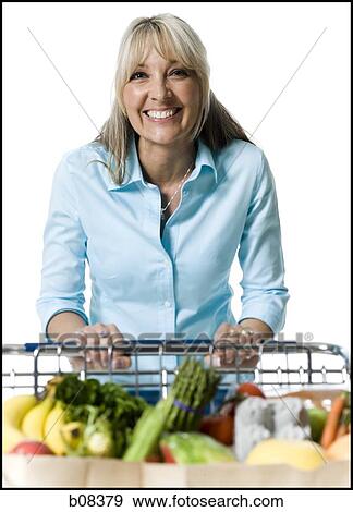 Portrait of an adult woman holding a shopping cart of vegetables and smiling View Large Photo Image Stock Photo - Portrait of an adult woman holding a shopping cart of vegetables and smiling. Fotosearch
