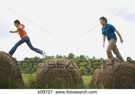 Profile of a man and his daughter leaping on hay bales View Large Photo Image Stock Photo - Profile of a man and his daughter leaping on hay bales. Fotosearch