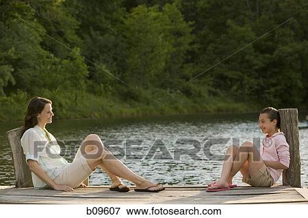 Profile of a woman and her daughter sitting face to face on a pier View Large Photo Image Stock Photo - Profile of a woman and her daughter sitting face to face on a pier. Fotosearch