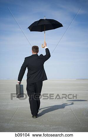 Rear view of a businessman walking and holding an umbrella View Large Photo Image Picture - Rear view of a businessman walking and holding an umbrella. Fotosearch