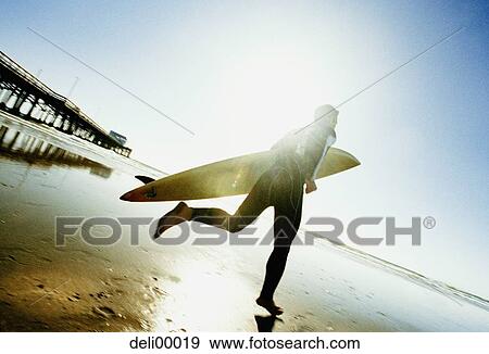 Rear view of a mid adult man holding a surfboard View Large Photo Image Stock Photo - Rear view of a mid adult man holding a surfboard. Fotosearch