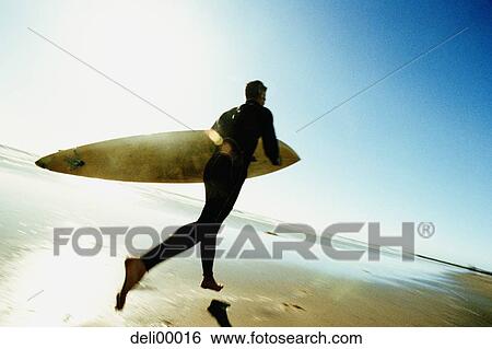 Rear view of a mid adult man holding a surfboard View Large Photo Image Stock Photograph - Rear view of a mid adult man holding a surfboard. Fotosearch