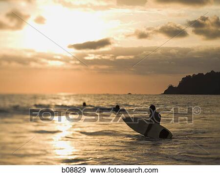 Rear view of a person holding a surfboard View Large Photo Image Stock Photo - Rear view of a person holding a surfboard. Fotosearch